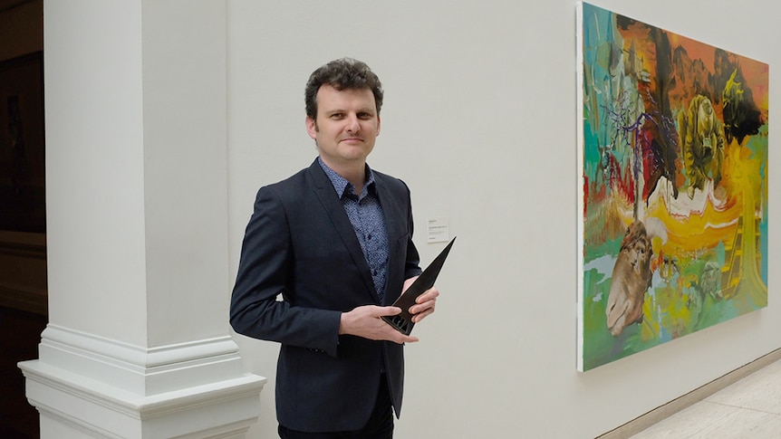 Slava Grigoryan holding the 2018 ARIA award standing next to a brightly coloured painting.