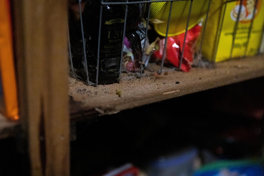 A wooden cupboard stacked with food, and filled with rat droppings and cobwebs.