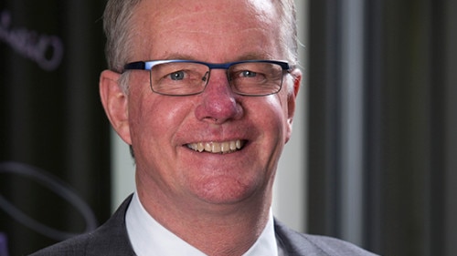 A bespectacled man wearing a dark suit, smiling.