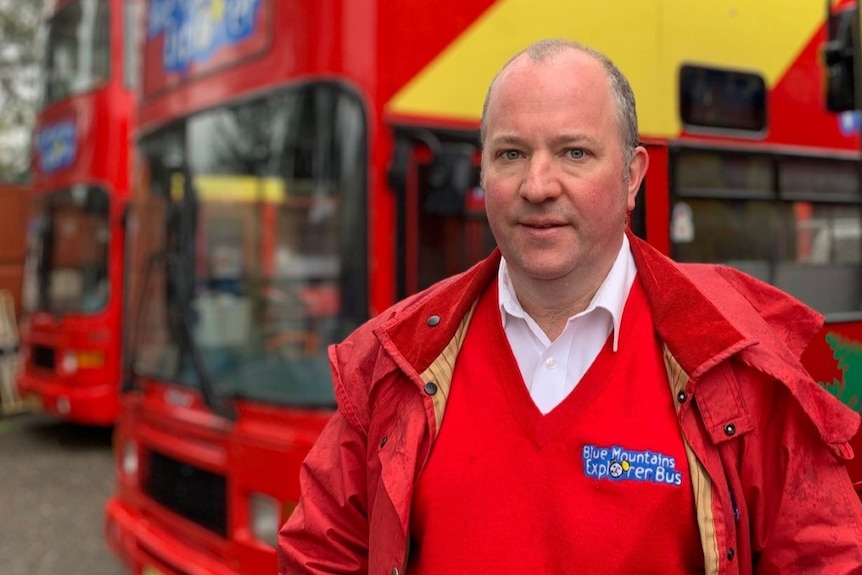 Jason Cronshaw stands in front of his buses in a car park.