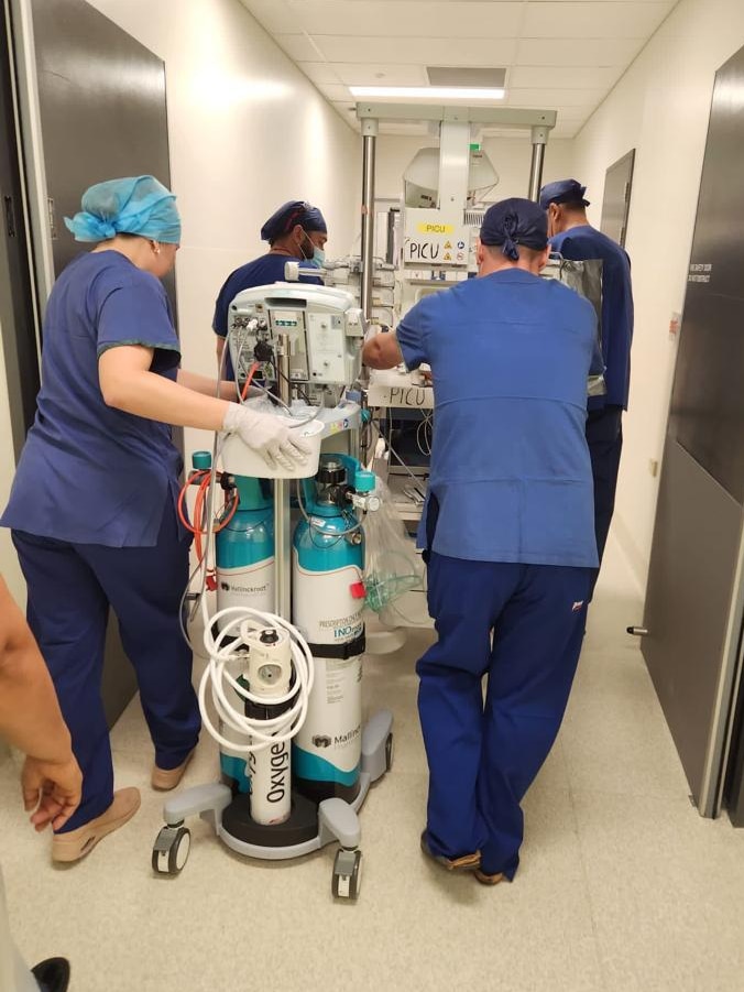 Medical staff in scrubs wheel a cot into surgery