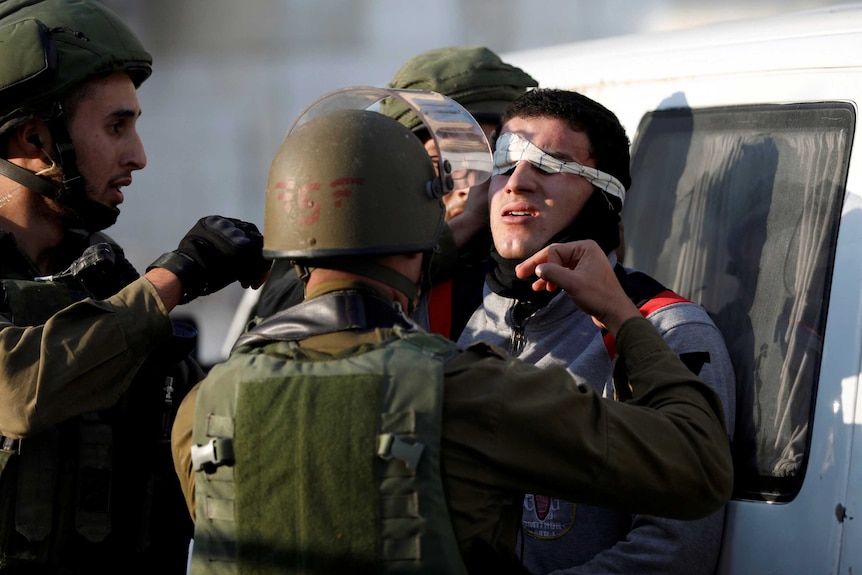 Israeli soldiers blindfold a Palestinian as they detain him during clashes with Israeli troops.