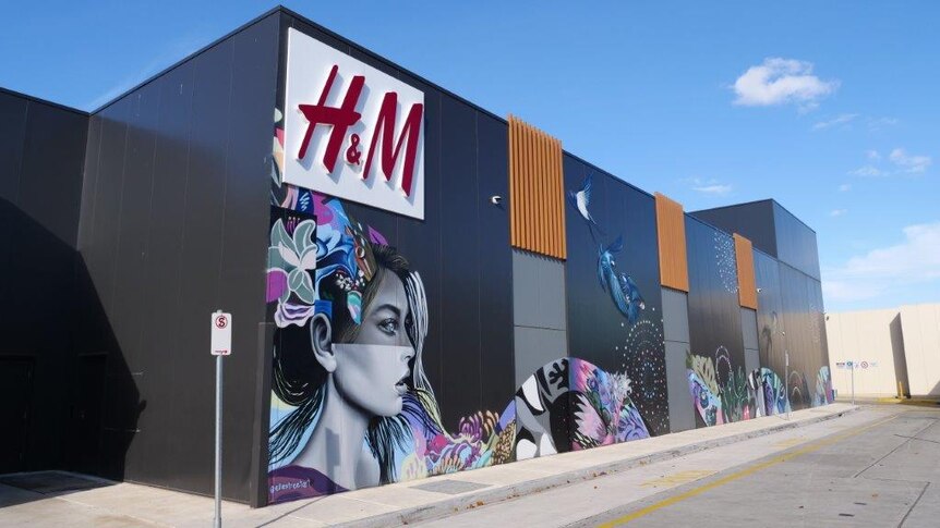 The outside of a shopping centre with an H&M logo and a mural of a woman.
