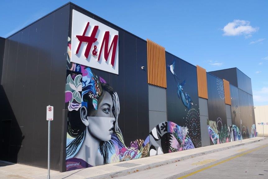 The outside of a shopping centre with an H&M logo and a mural of a woman.