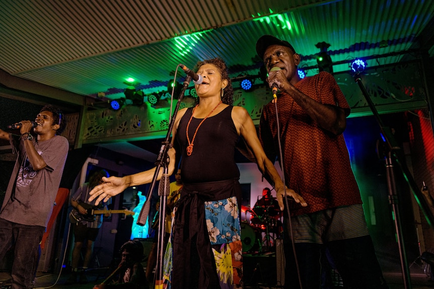 a woman and man sing on stage with a band