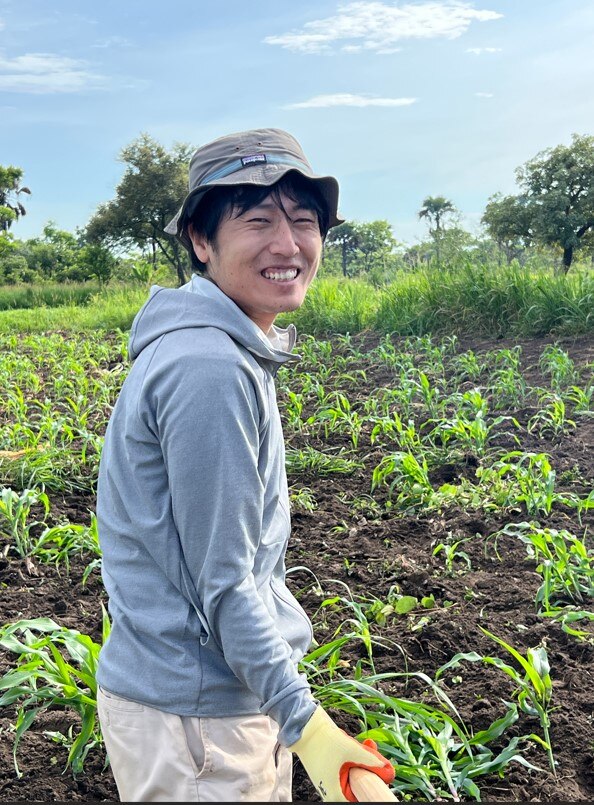 Un hombre japonés sonriente de pie en un campo de arroz.