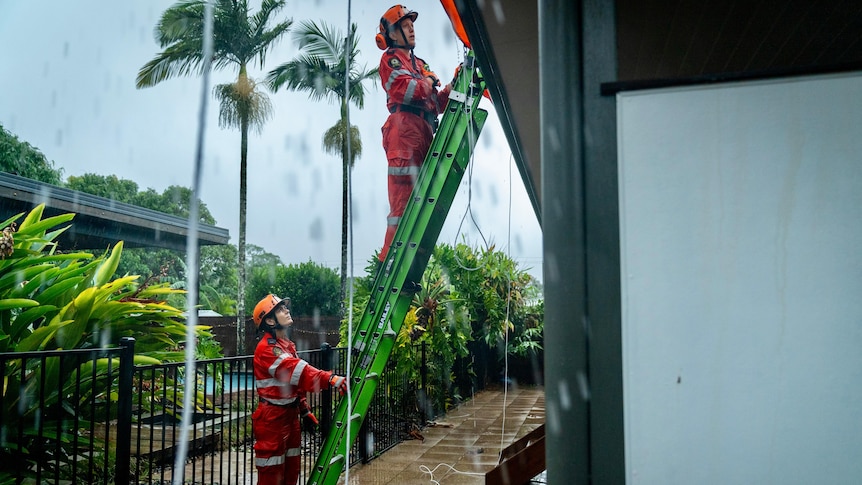 an ses worker holds a ladder while the other looks at a roof