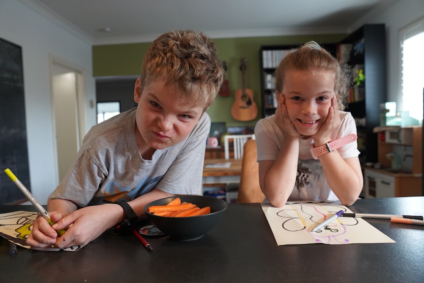 Two children draw, smiling.