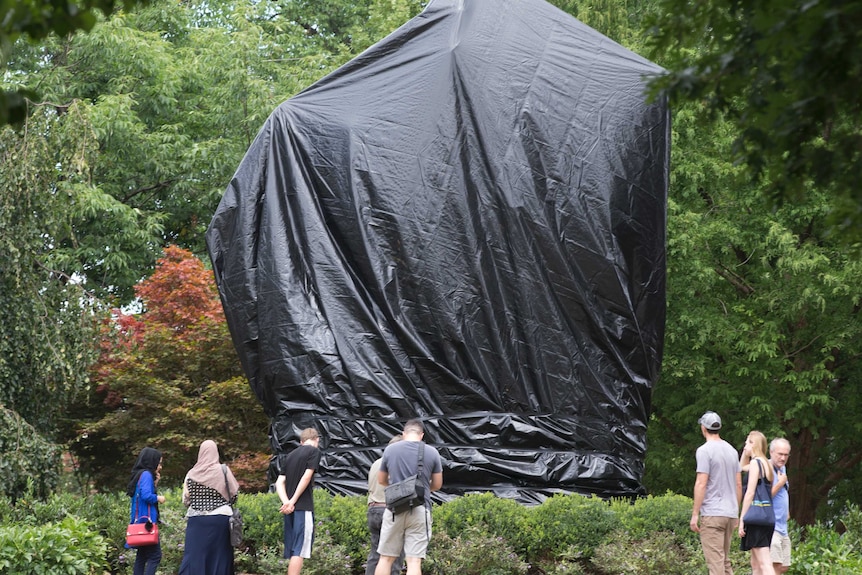 People look at a covered statue of Robert E Lee.