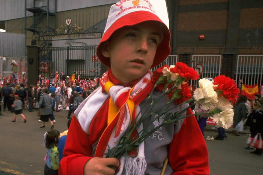 A young Liverpool fan carries flowers to lay in tribute at Anfield following the disaster.