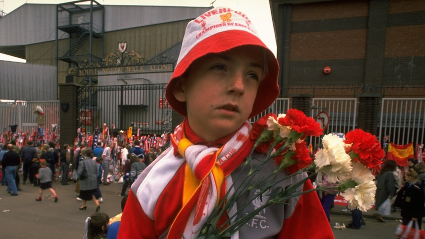 A young Liverpool fan carries flowers to lay in tribute at Anfield following the disaster.