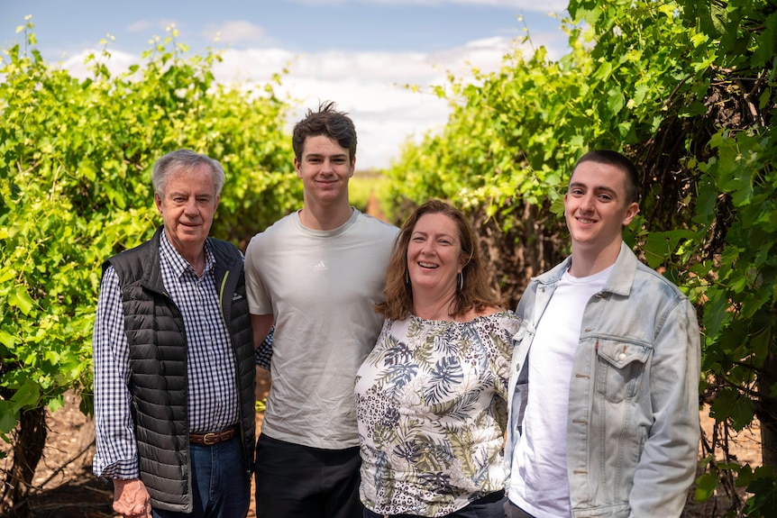 The Byrne family, an older man, a young man, a middle-aged woman, and young man stand smiling in their vineyards.