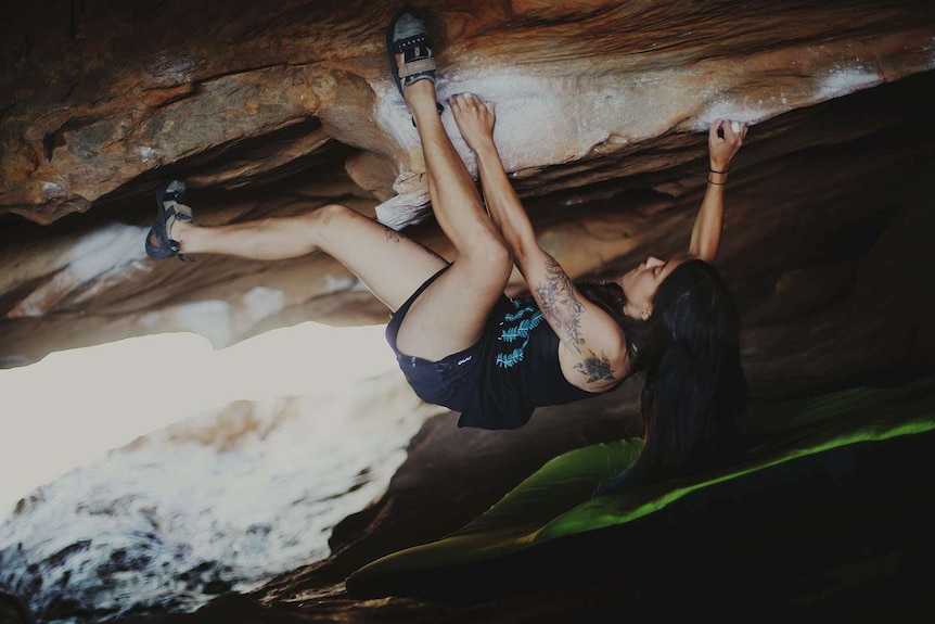 A rock climber hangs from a rock by their feet and hands