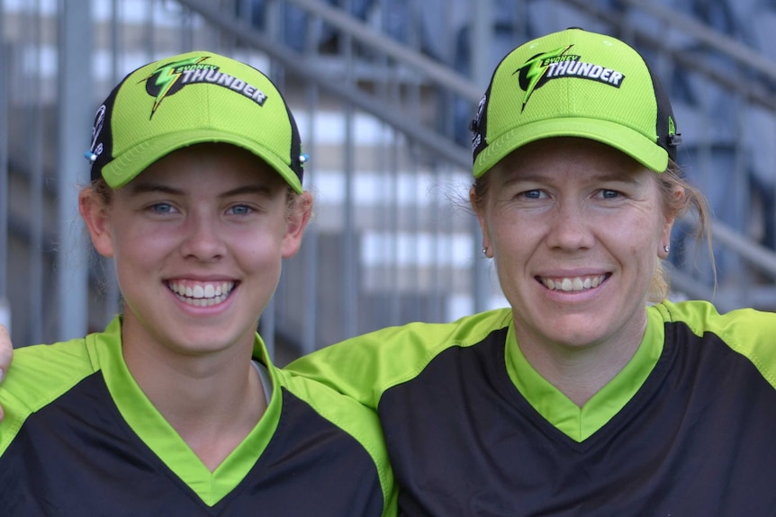 Two female cricketers smiling in their lime green and black caps