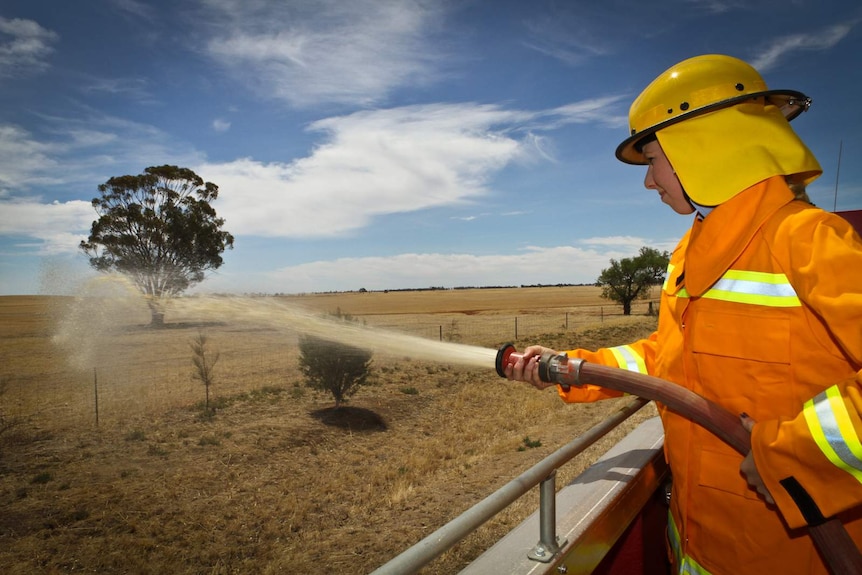 Young woman in yellow helmet and orange coast with fire hose