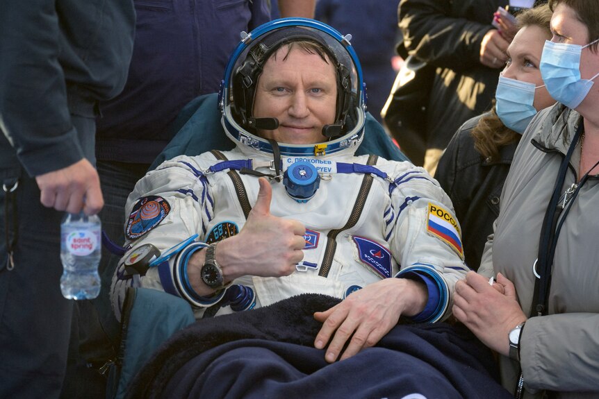 A man in a space suit gives a thumbs up/