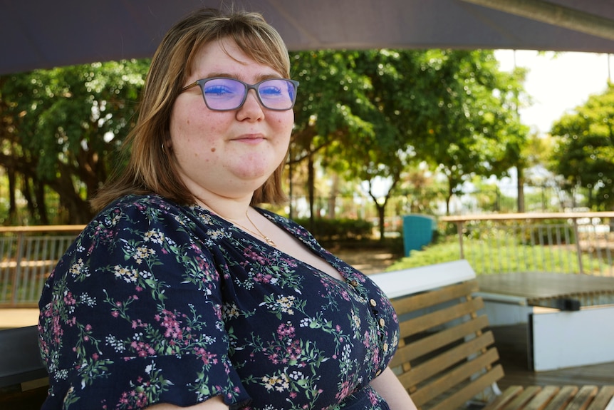 A woman in glasses sits on a bench in a park.