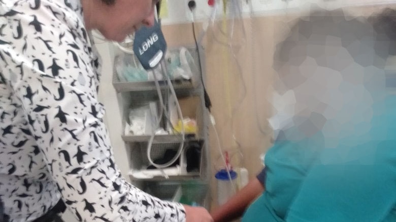 Photo of a teenage girl in handcuffs, sitting on a hospital bed while a woman in a white top leans towards her.