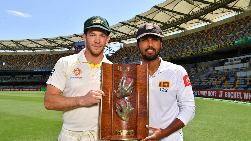 Two men stand holding a large, three panelled, wooden trophy in a cricket stadium