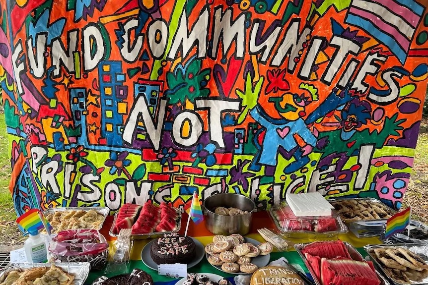 cakes, watermelon and sweets are laid out in front of a colour poster and decorated with the queer flag