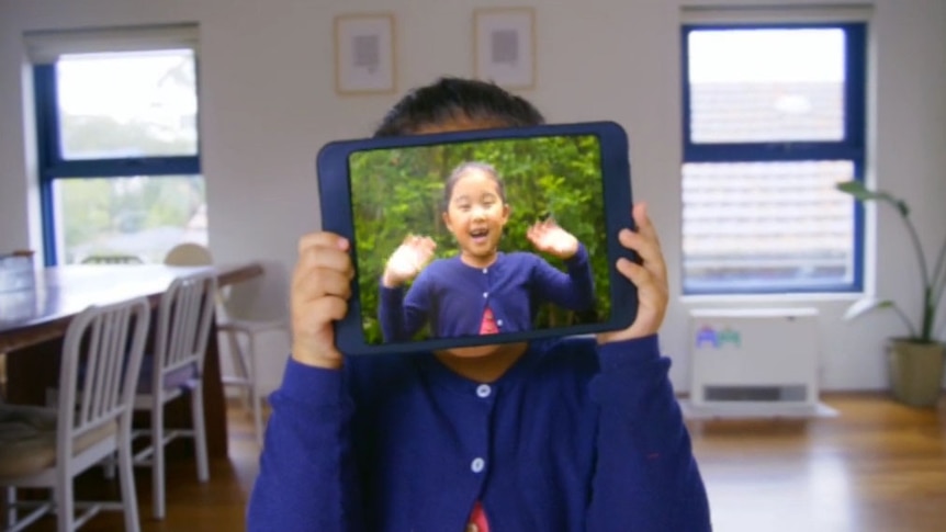 Young girl with tablet over her face with a video of herself playing on the tablet