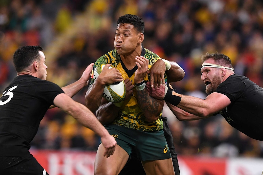 Israel Folau holding the ball in his right arm close to his chest as he tries to break a tackle from the All Blacks in Brisbane.