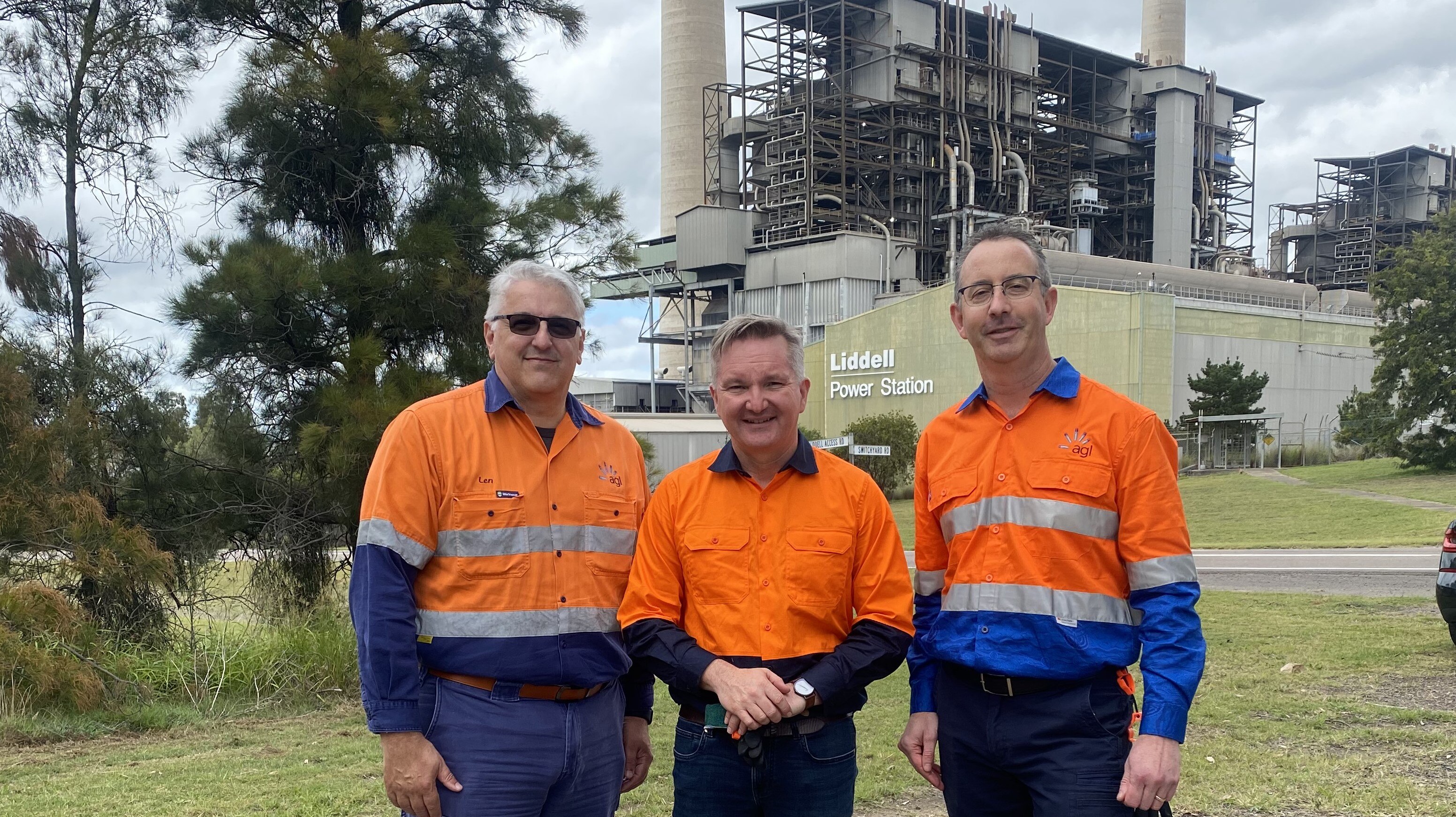 Three men in high-viz in front of a power station.