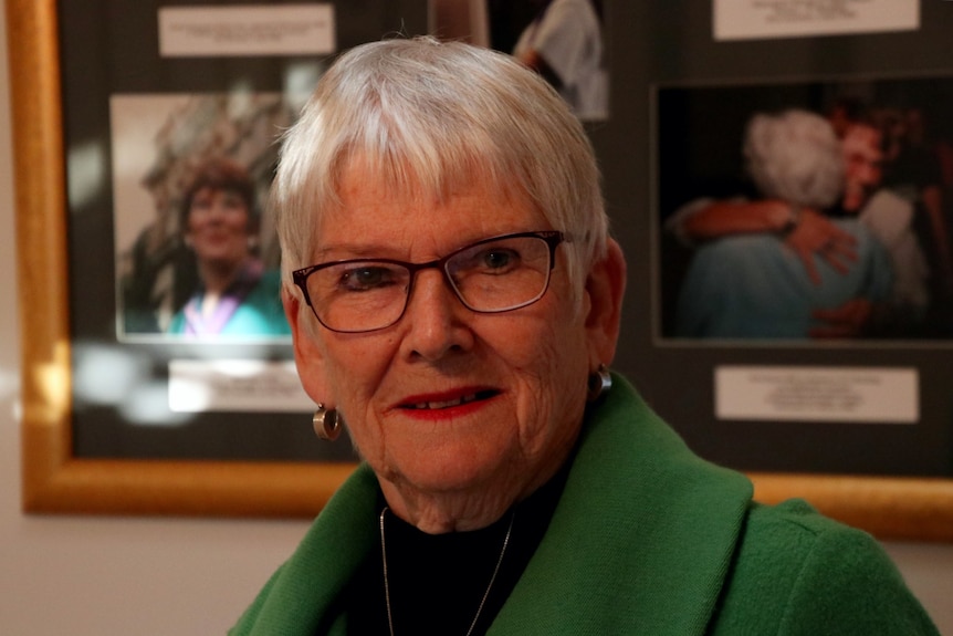 Ms Davenport stands in front of a photo board showing images of her as a younger woman.