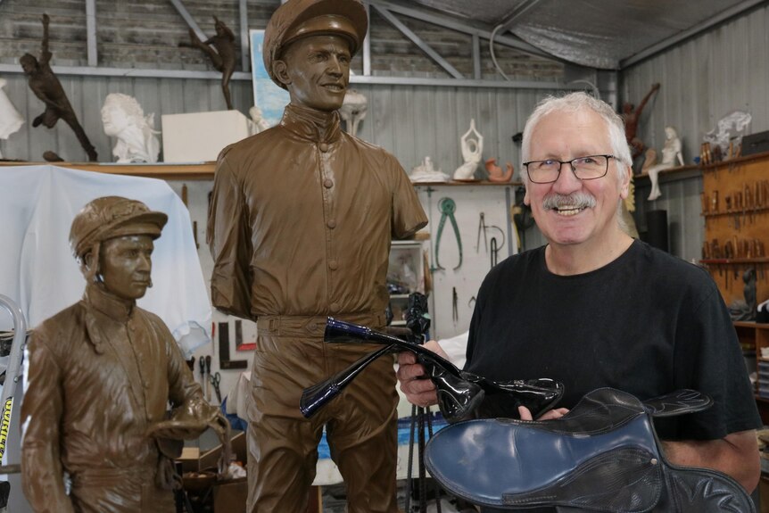 Two brown clay sculptures of jockey with helmet on and man holding black riding boots and jockey saddle.