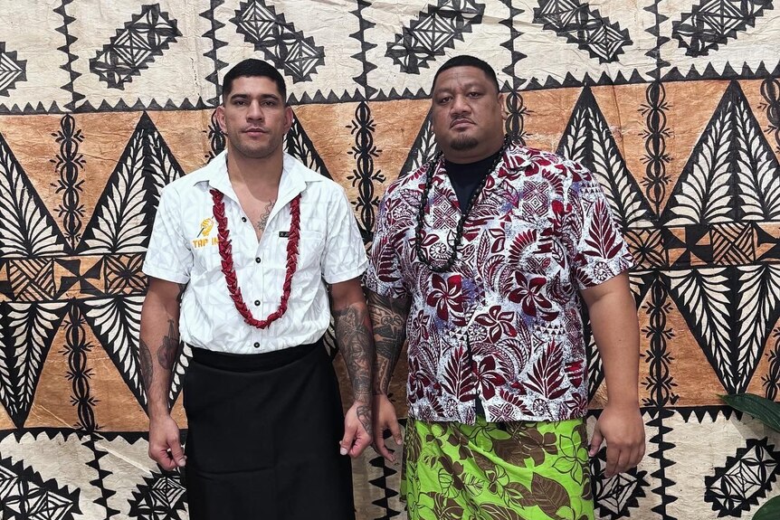 Two men standing next to each other dressed in traditional islander attire.