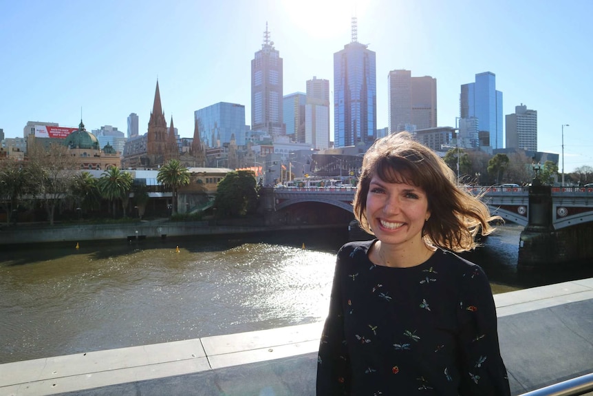 Gitta Scheenhouwer stands on Southbank with Flinders Street Station, St Paul's Cathedral and Melbourne's skyline behind her.