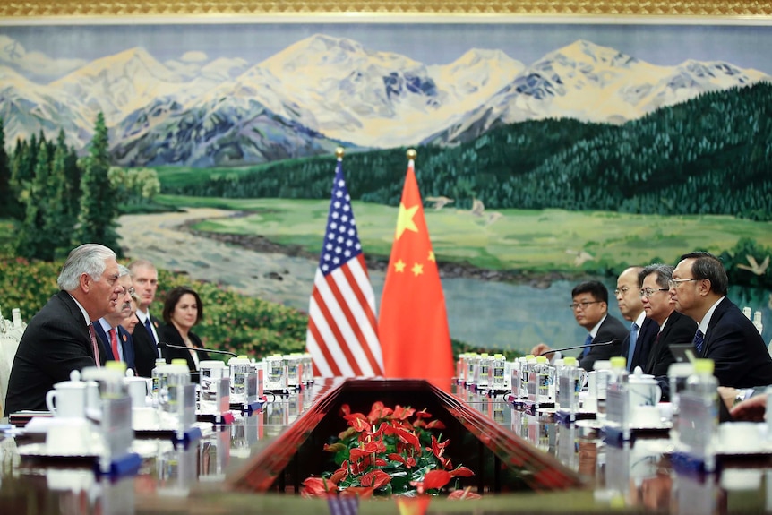 Rex Tillerson seated in the Great Hall of the People. There is a huge mural at one end of the table of mountains and a river.