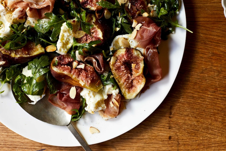 A close up of a plate with torn figs, mozzarella, prosciutto, rocket and nuts, a quick salad dinner.