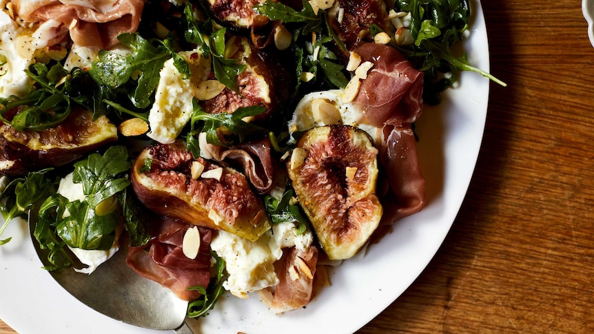 A close up of a plate with torn figs, mozzarella, prosciutto, rocket and nuts, a quick salad dinner.