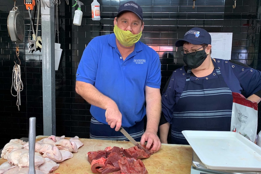 A man and a woman standing in a butcher shop, cutting up meat.