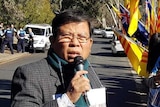 Chau Van Kham speaks at a protest in Canberra on 10 June 2018 with people holding yellow and red flags and signs.