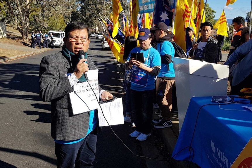 Chau Van Kham speaks at a protest in Canberra on 10 June 2018 with people holding yellow and red flags and signs.