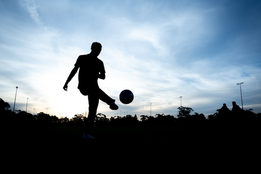 A silhouette of a soccer player kicking a ball on a field