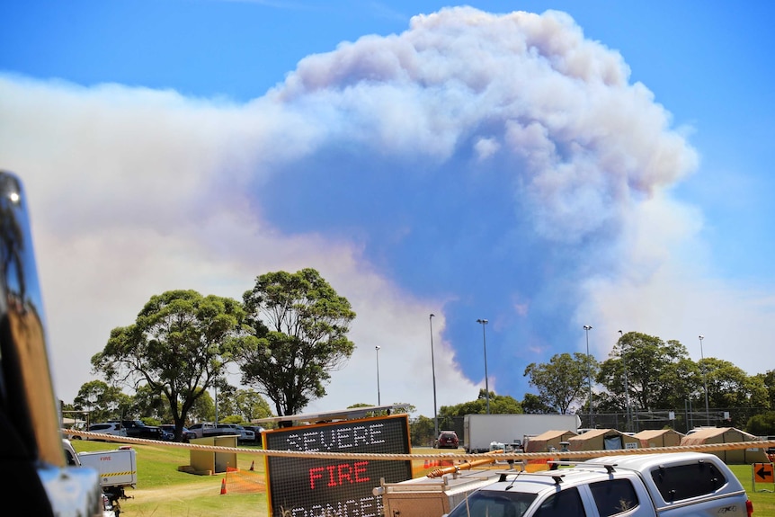 A plume of smoke stretches into the sky, behind a sign that says "severe fire danger" in a field.