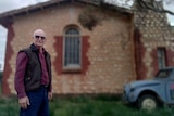 A senior man smiles as he stands in front of an old church building.