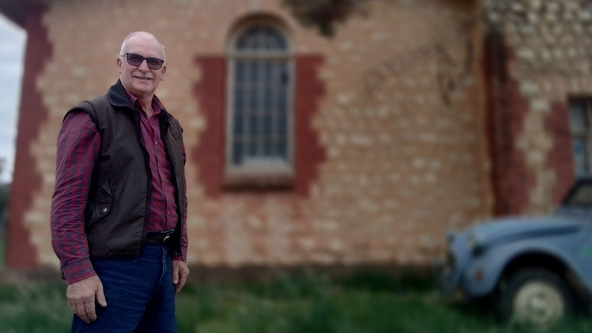 A senior man smiles as he stands in front of an old church building.