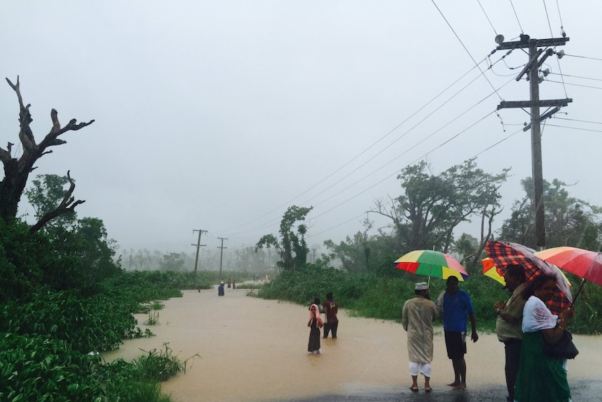People holding umbrellas look at the flooded bridge in the town of Ba in Fiji.