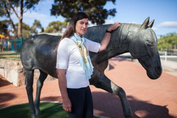 A woman in a white tshirt leans on a statue of a horse