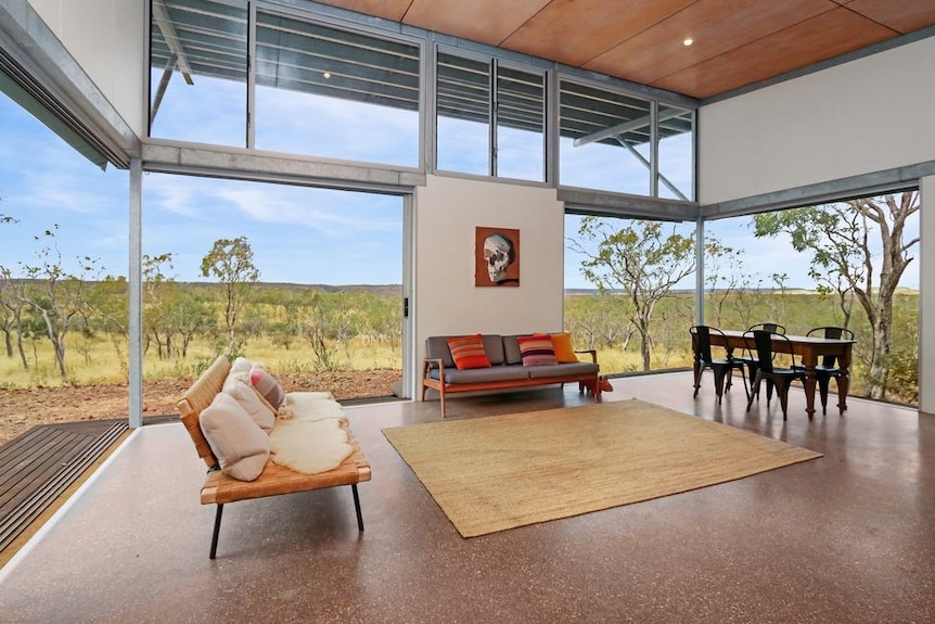 A striking view of flat spinifex plains can be seen through the wide glass windows of a light-filled living room.
