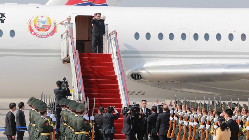 Kim Jong-un waves as he prepares to walk down steps covered in red carpet from a plane.