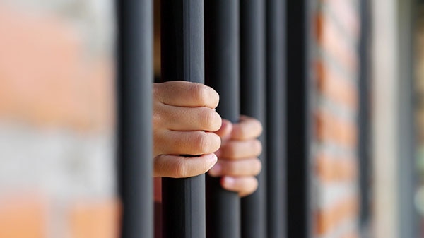 Photo of hands gripping onto prison bars.