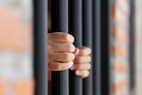 Photo of hands gripping onto prison bars.