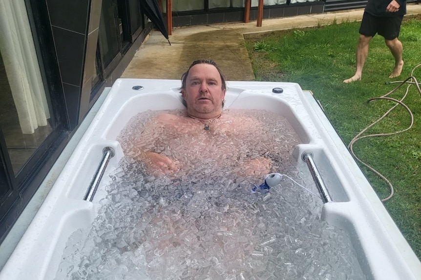 A man lies in a bath tub outdoors filled with ice and cold water