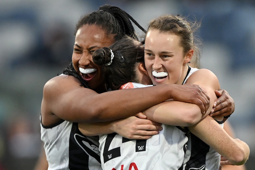 Three Collingwood AFLW players embrace as they celebrate a goal.