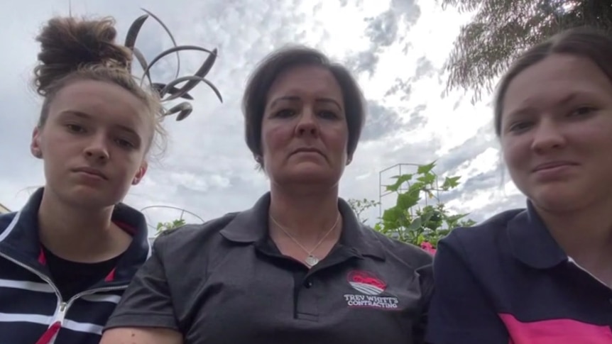 A woman with two girls speaking down to a camera looking upset